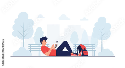 Boy Relaxing In The Park Using Tablet Computer With Backpack Next To Him