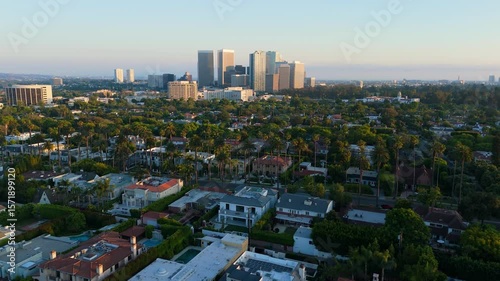 Drone flying forward over Beverly Hills homes toward Century City skyline at golden hour