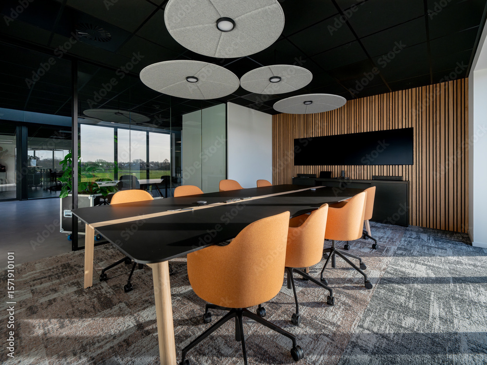 Fototapeta premium Modern conference room with orange chairs, black table, wood accent wall, and circular ceiling lights