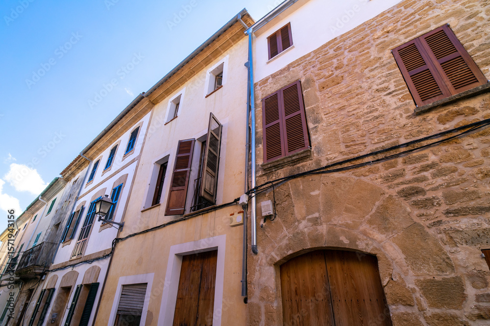 Fototapeta premium A narrow, old street in a Mediterranean country. Wooden doors and windows with wooden shutters, and balconies. Alcúdia, Mallorca, Balearic Islands, Spain. An island in the Mediterranean Sea. 