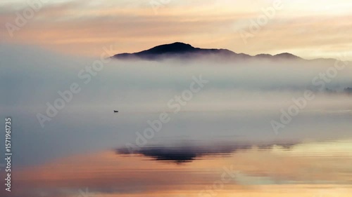 Footage of misty mountains by a lake at sunrise.