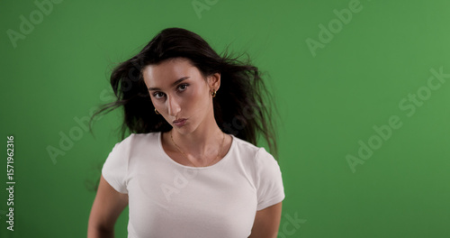 Studio shot of a young woman with blowing hair posing on a green screen background