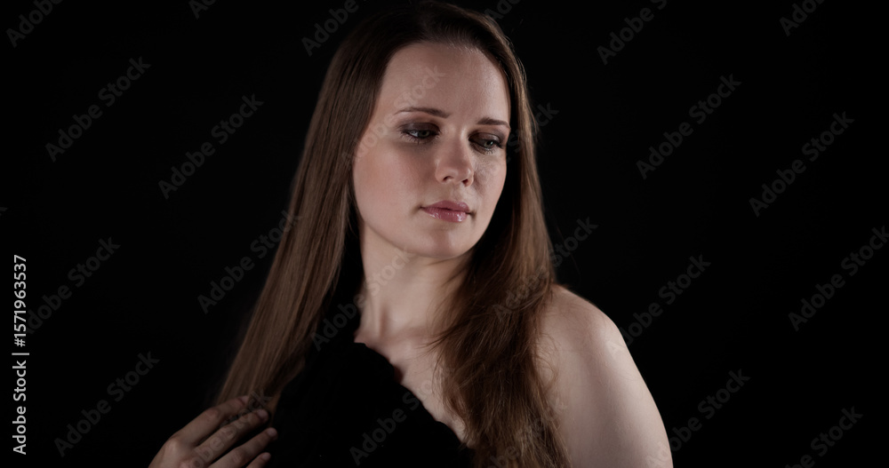 Fototapeta premium Pensive young woman with long brown hair looking away on black background