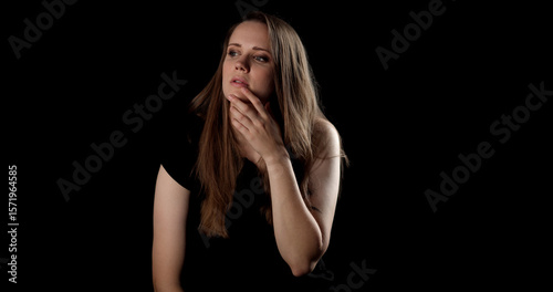 Studio portrait of a thoughtful young woman with hand on chin looking away on a dark background