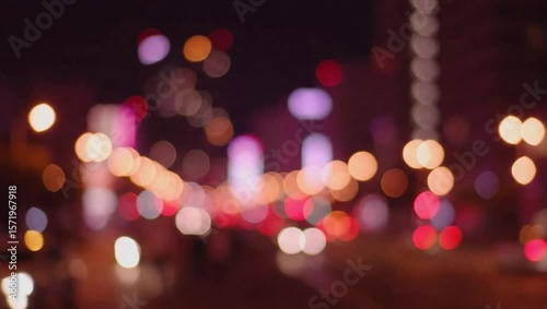 Blurred city lights at night create a colorful bokeh effect on the road.