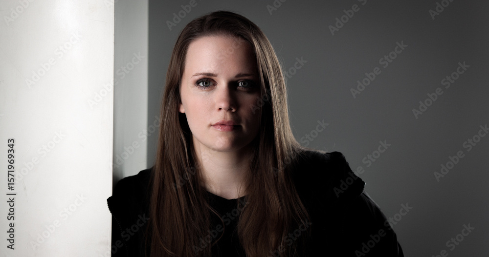 Fototapeta premium Studio portrait of a young woman with long brown hair wearing a black shirt, posing near a white wall
