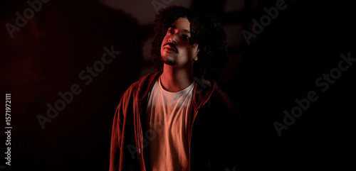 Portrait of a stylish young man with curly hair looking up, illuminated by a red light in a dark room