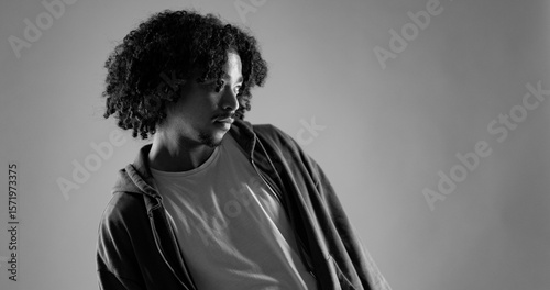 Studio portrait of a young african american man with curly hair wearing casual clothes, looking away in black and white