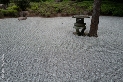 Zen garden with carefully raked gravel circles around a stone lantern and tree. A peaceful, meditative scene that embodies harmony and Japanese minimalism.