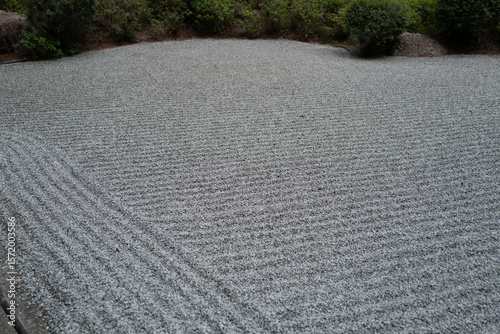 Close-up of a meticulously raked gravel surface in a Zen garden, showing textured parallel lines and subtle light play. A calm, meditative and abstract visual.
