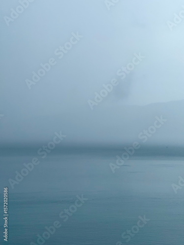 Misty seascape on a foggy day. Calm water and sky blending on the horizon. Minimalist and atmospheric nature background.