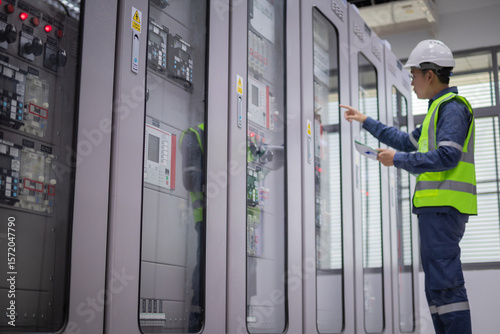 Engineer wearing safety helmet and reflective vest performs inspection on electrical relay panels inside substation to ensure protection and proper operation of equipment