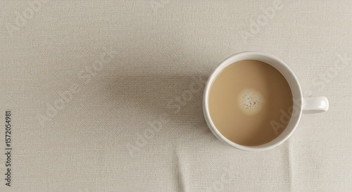 High angle view of a cup of milk tea with foam on a textured neutral surface