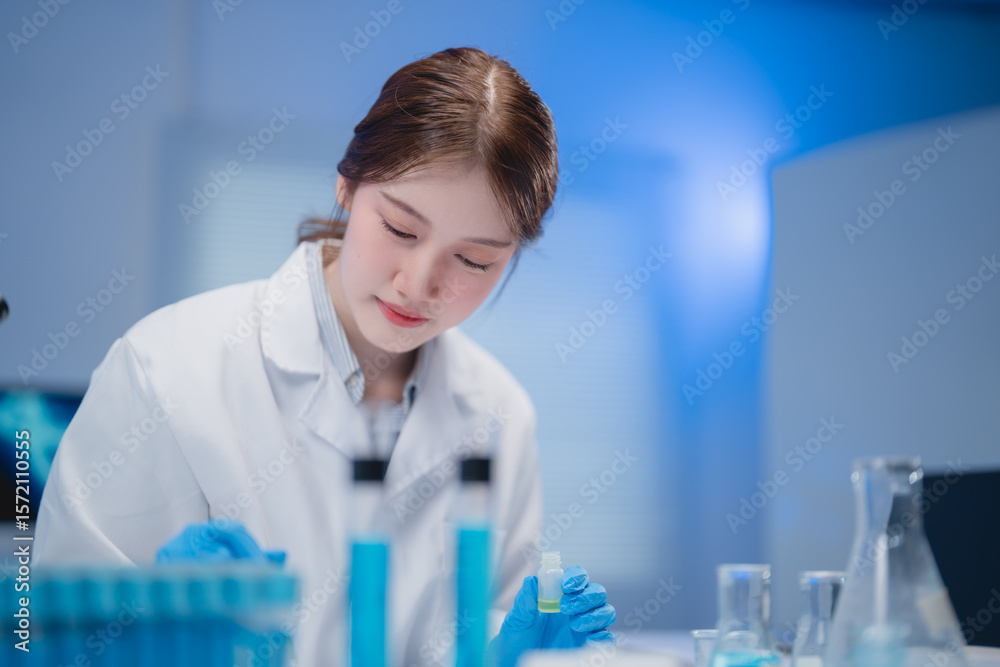 Fototapeta premium Focused young scientist in a laboratory setting, conducting experiments with test tubes and beakers. Wearing a lab coat and gloves, she demonstrates precision and concentration in her work