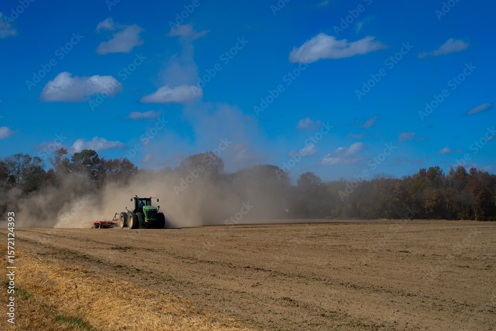 Naklejka premium Tractor ploughing the field. Autumn farming in the countryside. Tractor on rural farmland. Agricultural machine or tractor working on soil. Tractor plowing ground for cultivation. Farm soil ground.
