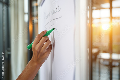 A hand writing on a whiteboard with a green marker in a bright office space
