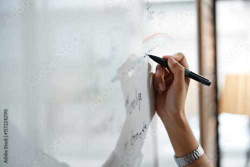 A person writing on a whiteboard with a black marker in a bright environment