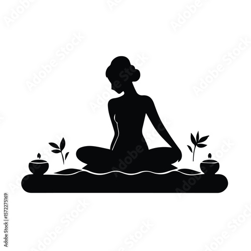 Female silhouette meditating in a spa setting. Relaxed seated pose on a water feature with candles and plants. Female spa client in a tranquil spa location -