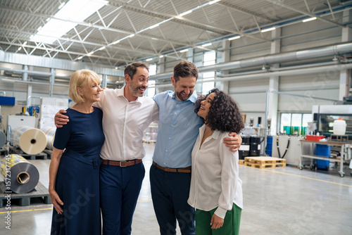 Happy business colleagues standing with arms around each other at factory
