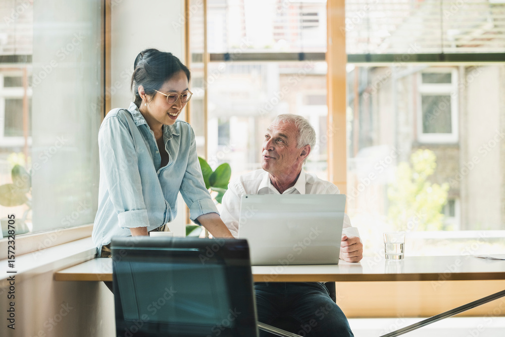 Smiling businessman with colleague discussing work in office Smiling businessman with colleague discussing work in office
