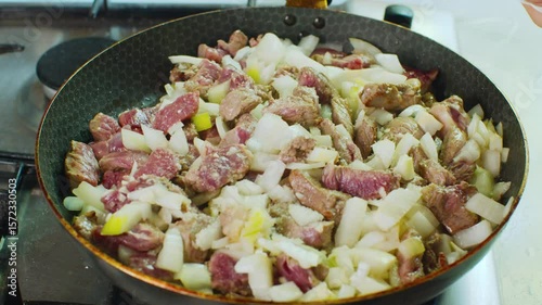 Sprinkling salt over a meat and onion dish in a black frying pan during cooking