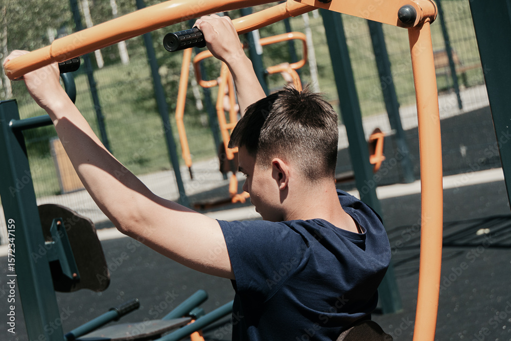 Obraz premium Young man exercising on outdoor gym equipment. Fitness workout in summer park.