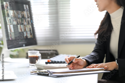 Businesswoman attending a virtual meeting, taking notes while focused on computer screen