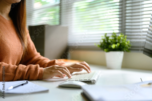 Close up of woman typing on wireless keyboard at a bright home office desk with natural light