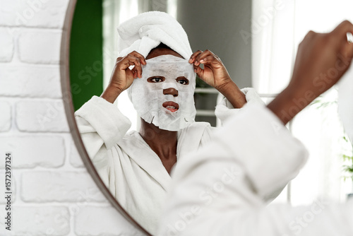 Woman applies a facial mask while looking in the mirror at home during a self-care routine