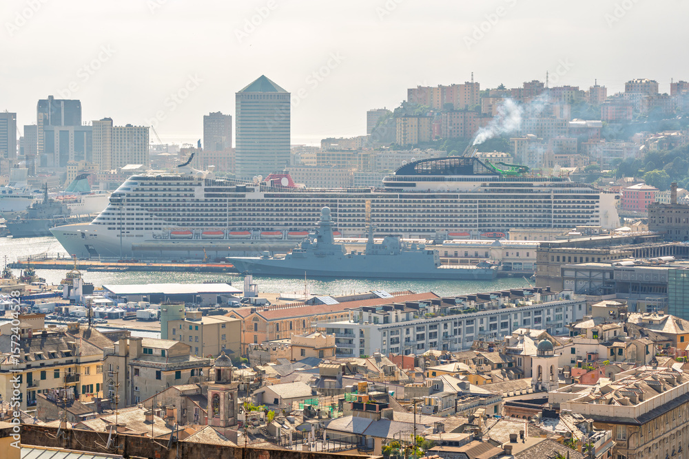 Obraz premium Genoa, Italy. A large cruise ship and military vessel dock side by side in the Port of Genoa, seen above the rooftops of the historic center