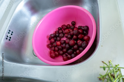 washed cherries in a pink plastic bowl in a stainless steel sink