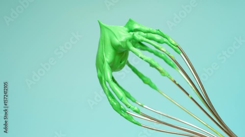 Whisk with green whipped cream from proteins close-up on blue background.