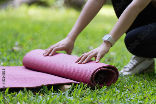 Yoga mat preparation. Close-up of hands rolling yoga mat on grass.