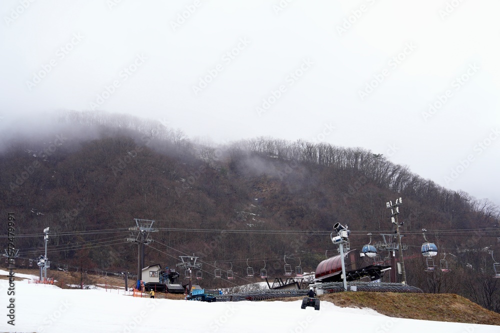Obraz premium Hakuba Goryu Snow Resort is a popular ski resort located in the Hakuba Valley, Nagano.Winter Sports Park at the top of the mountain snowy slope, patches of brown grass in late autumn Several ski lift.