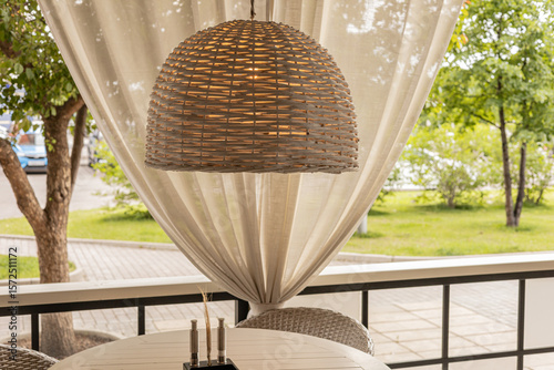 A tranquil outdoor area with a woven rattan pendant lamp, draped curtains, and lush garden views, ideal for gatherings, meals, relaxation.