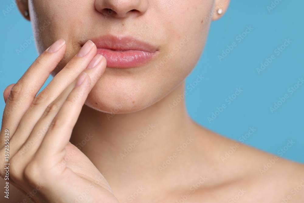 Obraz premium Young woman with lip balm on her lips against light blue background, closeup