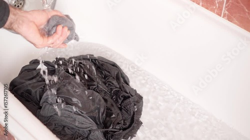 Washing black clothes in a bathtub using water and detergent for effective cleaning