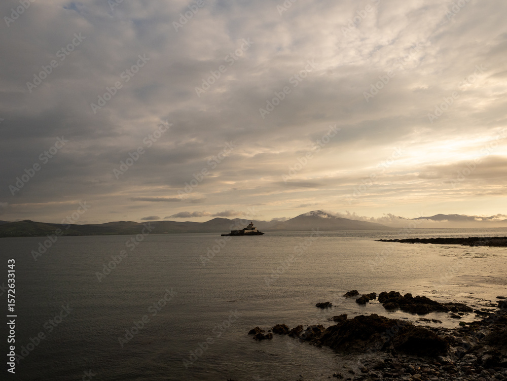 Fototapeta premium A calm sea reflects the soft golden light of dusk, with a solitary lighthouse on a distant islet