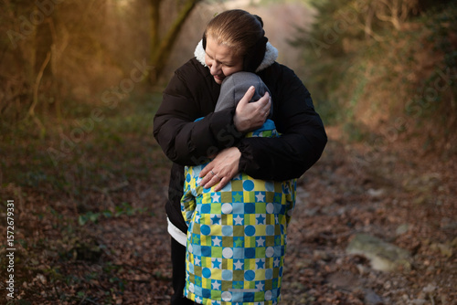 A warm hug between a mother and child, standing along a serene woodland trail, emphasizing feelings of love, care, and bonding in nature. Son and mother hugging and talking in nature
