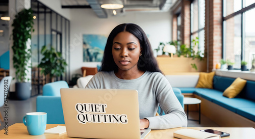 A young female employee personifies the quiet quitting trend, working with a sticker on her laptop in a modern office.