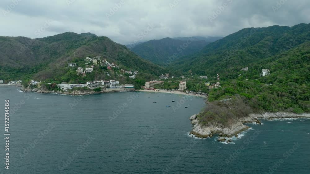 Panoramic aerial approach to Mismaloya coastline with hills and bay framed by tropical foliage in foreground Panoramic aerial approach to Mismaloya coastline with hills and bay framed by tropical foliage in foreground