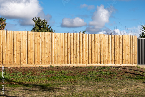 A newly installed vertical timber fence with neatly aligned wooden palings in a suburban backyard. a classic and modern boundary in Australian residential properties.