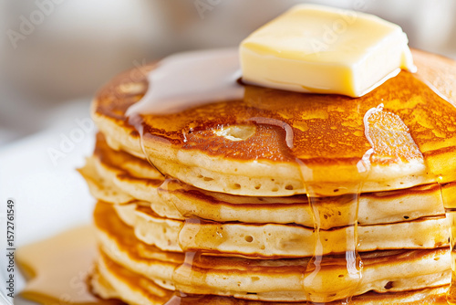 A stack of fluffy pancakes with syrup dripping and a dollop of butter on top