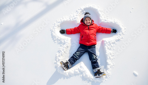 Young boy making snow angel while smiling in winter snow  