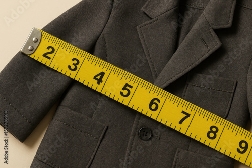 Tailored dark blazer for children measured with yellow tape for precise fit on neutral background, showcasing custom garment sizing