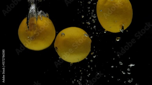 Slow motion three yellow lemon falling into transparent water on black background. Fresh fruits splashing in aquarium. Citrus, food, air bubbles