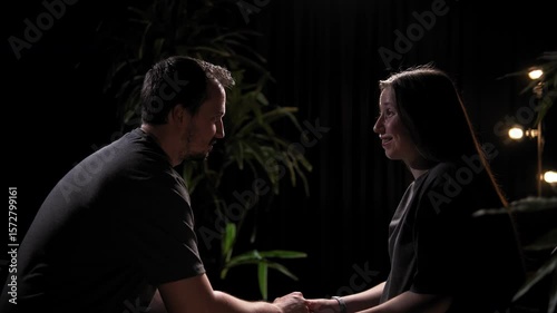 Husband and his wife are sitting opposite each other in a dark room and talking