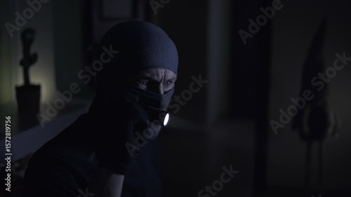 A thief with a flashlight in a dark room answers a call on his smartphone
