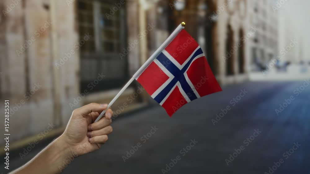 Hand holding norwegian flag in urban street setting captures scandinavian patriotism with red white blue colors.