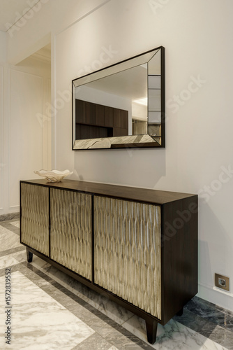 Картината върху платно A stylish wooden sideboard with textured gold doors and a beveled mirror above